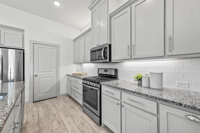 kitchen with decorative backsplash, light hardwood / wood-style floors, light stone counters, and stainless steel appliances