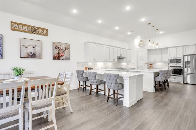 kitchen featuring hardwood / wood-style flooring, pendant lighting, a breakfast bar, white cabinetry, and appliances with stainless steel finishes