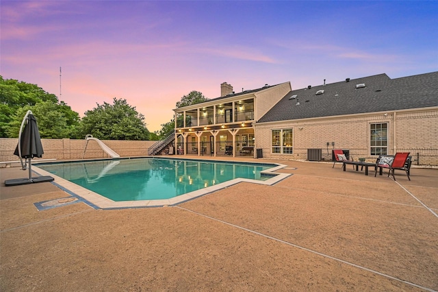 pool at dusk featuring a patio area, central air condition unit, and a water slide