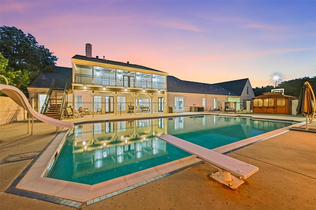 pool at dusk featuring a diving board, a patio area, and a water slide