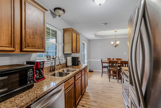 kitchen with sink, stainless steel appliances, a notable chandelier, a textured ceiling, and light wood-type flooring