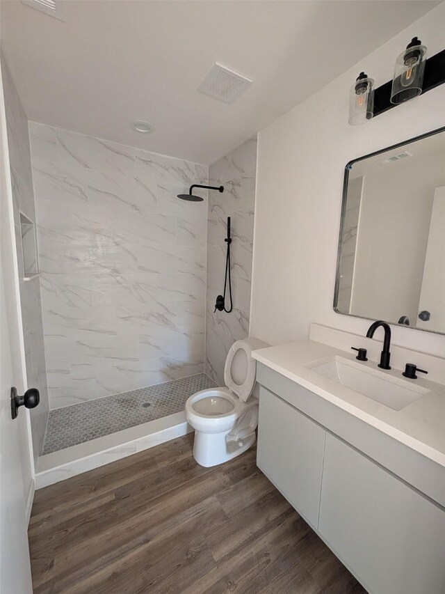 bathroom featuring tiled shower, vanity, hardwood / wood-style flooring, and toilet