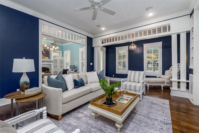 living room with ceiling fan with notable chandelier, dark hardwood / wood-style flooring, crown molding, and a brick fireplace