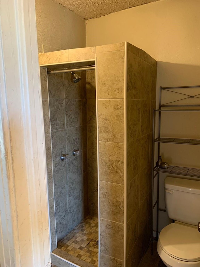 bathroom with a textured ceiling, toilet, and tiled shower