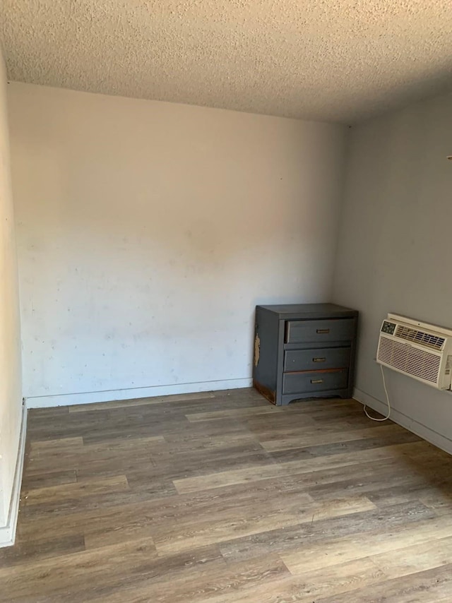 empty room featuring light wood-type flooring, a textured ceiling, and a wall mounted air conditioner