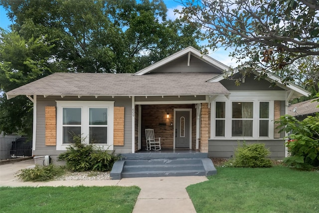 bungalow-style home with covered porch, roof with shingles, fence, and a front lawn