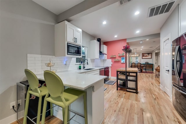 kitchen with black refrigerator, stainless steel microwave, white cabinetry, kitchen peninsula, and light wood-type flooring