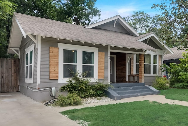 view of front of home with covered porch, a shingled roof, and fence