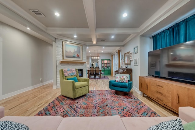 living room featuring beamed ceiling, a large fireplace, and light hardwood / wood-style flooring