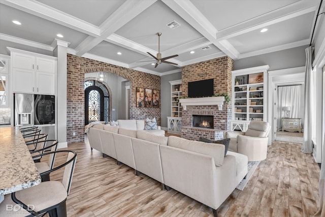 living room with beamed ceiling, a brick fireplace, coffered ceiling, and light wood-type flooring