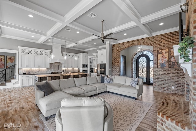 living room with brick wall, beamed ceiling, french doors, coffered ceiling, and light hardwood / wood-style flooring