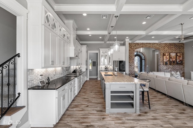 kitchen with a spacious island, a breakfast bar, hanging light fixtures, dark stone countertops, and white cabinets