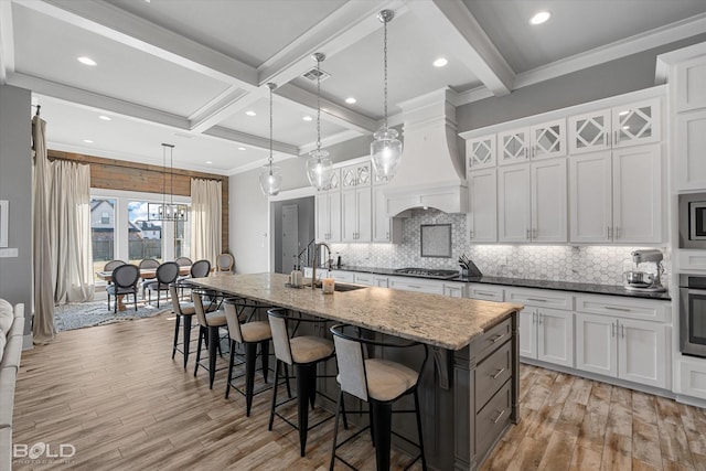 kitchen with pendant lighting, premium range hood, white cabinetry, dark stone countertops, and a center island with sink