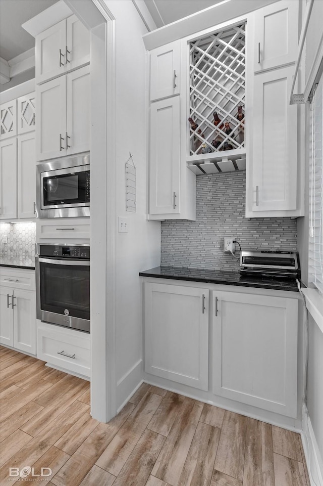 kitchen with backsplash, white cabinetry, light wood-type flooring, and appliances with stainless steel finishes