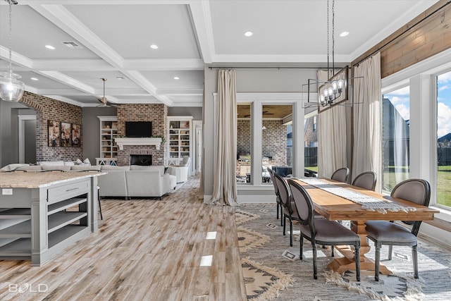 dining room featuring beamed ceiling, coffered ceiling, light hardwood / wood-style floors, crown molding, and a brick fireplace