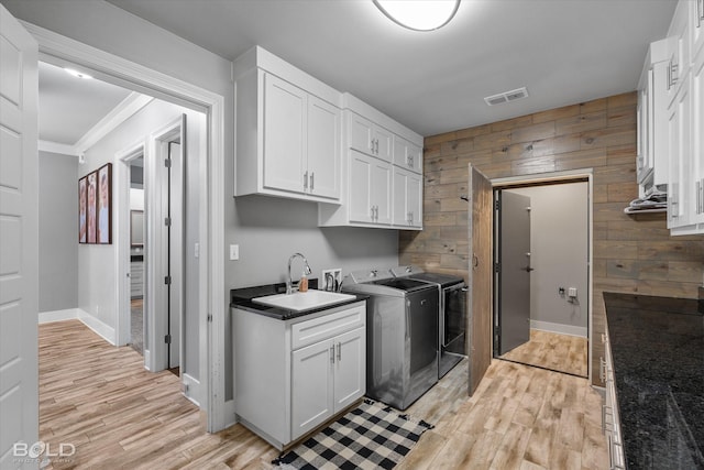 clothes washing area featuring wooden walls, sink, cabinets, and light hardwood / wood-style flooring