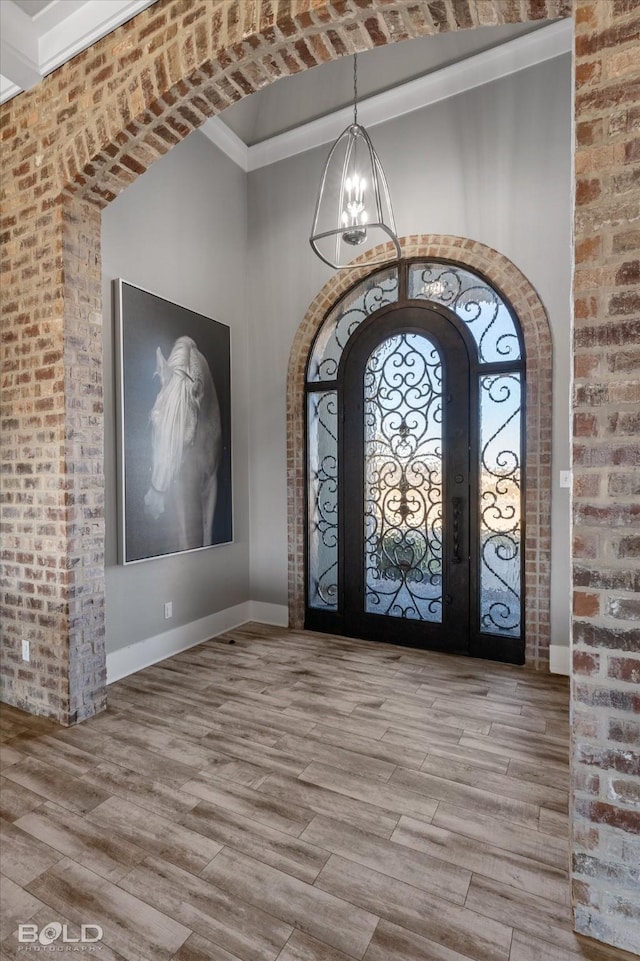 entryway featuring wood-type flooring, a chandelier, and brick wall