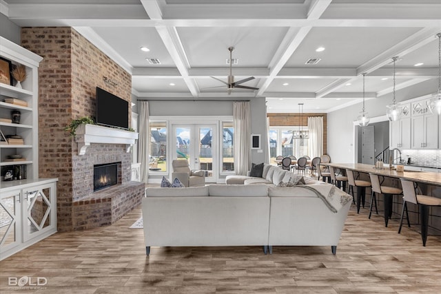 living room featuring ceiling fan, coffered ceiling, beamed ceiling, a fireplace, and light wood-type flooring