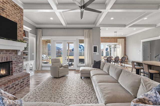 living room with ceiling fan, beamed ceiling, wood-type flooring, and a brick fireplace