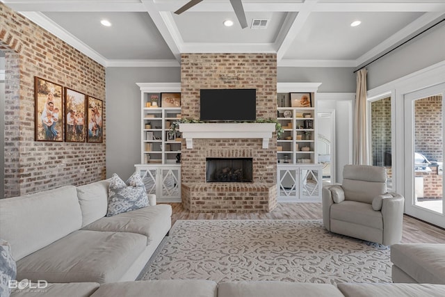 living room with brick wall, coffered ceiling, crown molding, a brick fireplace, and light hardwood / wood-style flooring