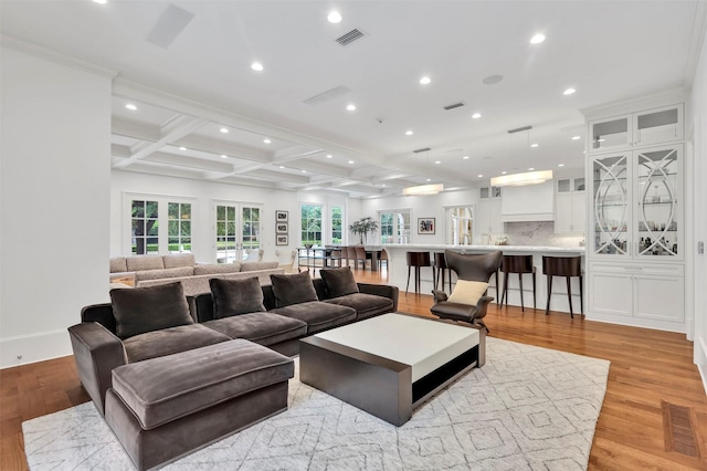 living room featuring beamed ceiling, light wood-type flooring, crown molding, and coffered ceiling