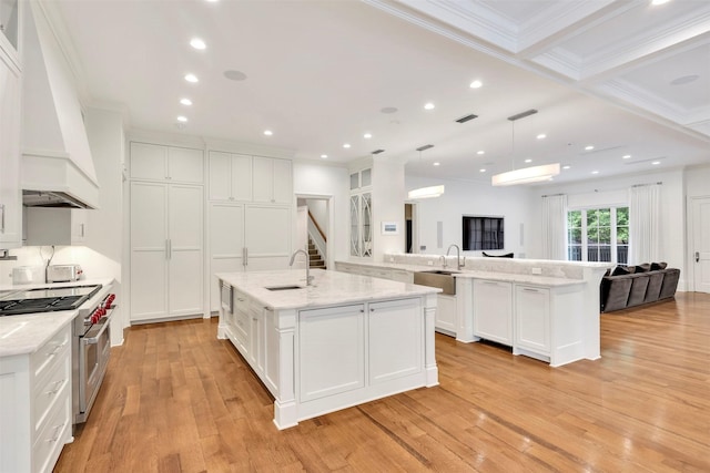 kitchen with a large island with sink, pendant lighting, range with two ovens, and custom exhaust hood