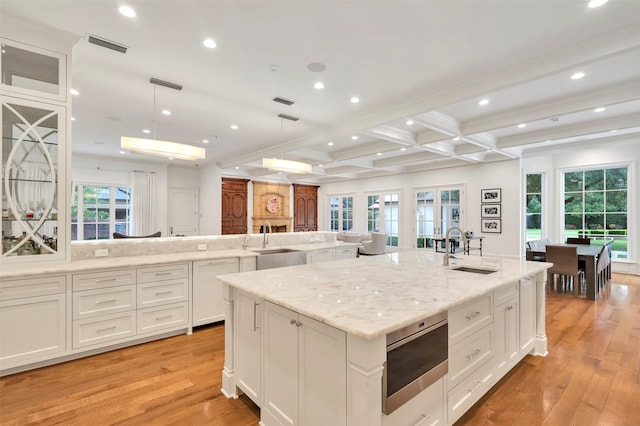 kitchen with a large island, sink, hanging light fixtures, beam ceiling, and light stone counters