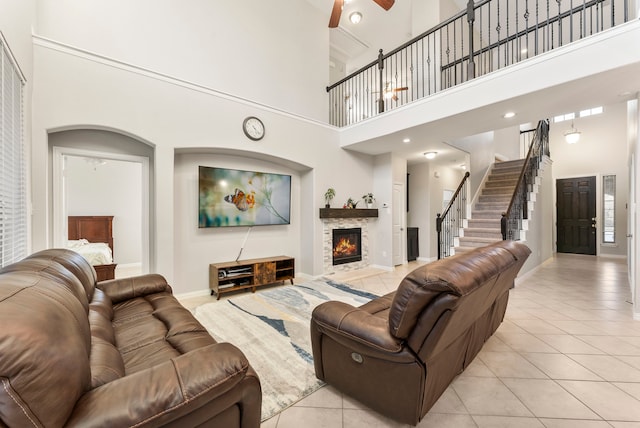 living room featuring ceiling fan, a towering ceiling, a fireplace, and light tile patterned floors