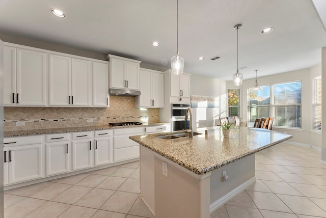 kitchen with light stone countertops, stainless steel appliances, white cabinetry, hanging light fixtures, and an island with sink