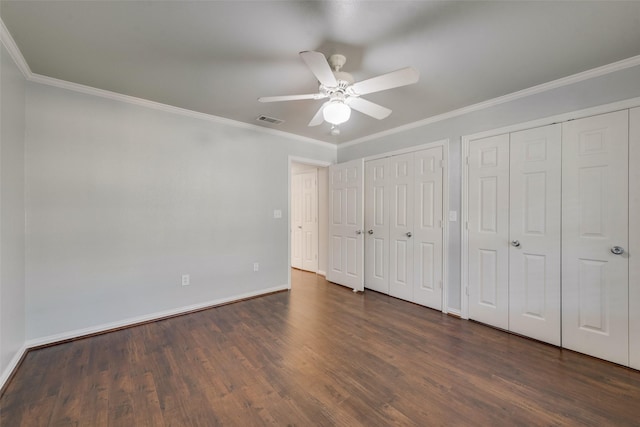 unfurnished bedroom with ceiling fan, dark hardwood / wood-style floors, ornamental molding, and two closets