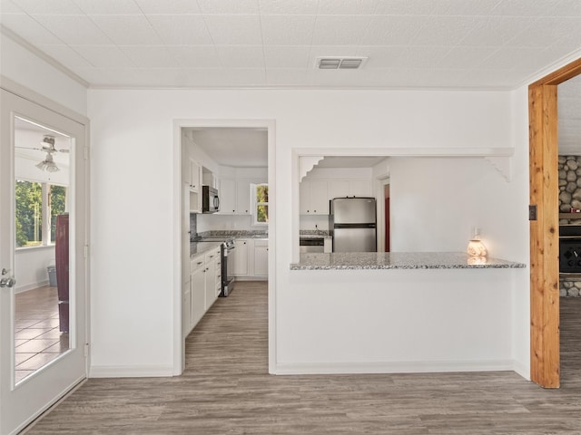 kitchen with light stone counters, appliances with stainless steel finishes, light hardwood / wood-style floors, white cabinets, and ornamental molding