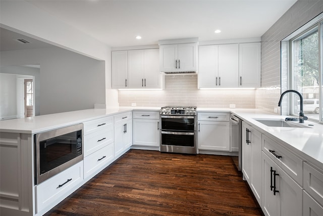 kitchen featuring white cabinets, a peninsula, stainless steel appliances, light countertops, and a sink