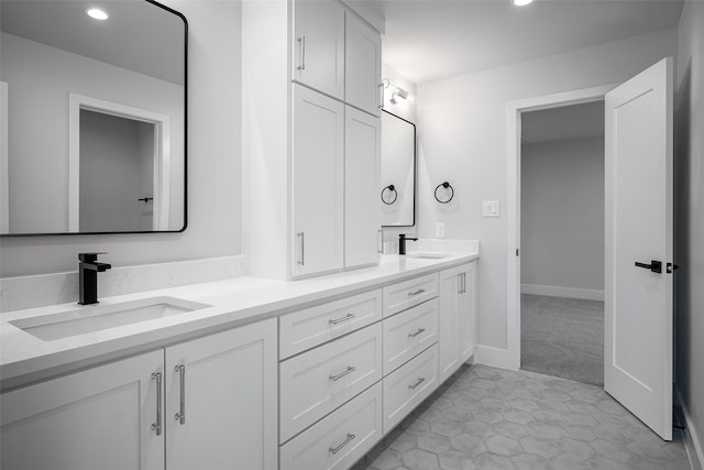 bathroom featuring baseboards, double vanity, a sink, and recessed lighting