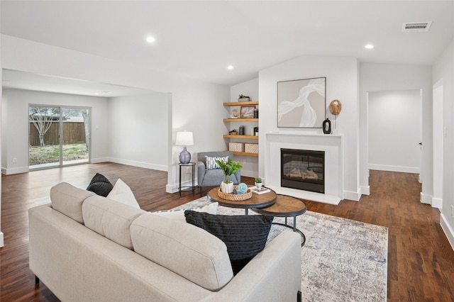 living area featuring baseboards, visible vents, a glass covered fireplace, dark wood-style floors, and vaulted ceiling