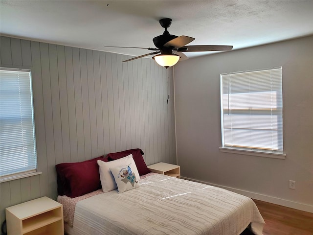 bedroom with hardwood / wood-style flooring, ceiling fan, and wooden walls