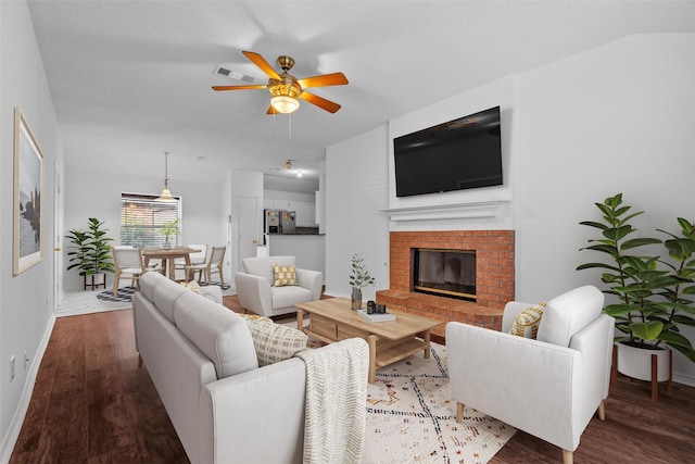 living room featuring vaulted ceiling, wood-type flooring, a brick fireplace, and ceiling fan