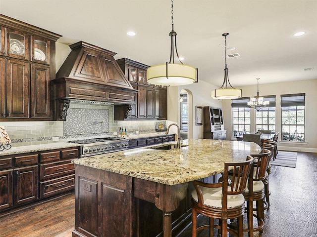 kitchen featuring backsplash, a kitchen island with sink, dark wood-type flooring, custom range hood, and dark brown cabinetry