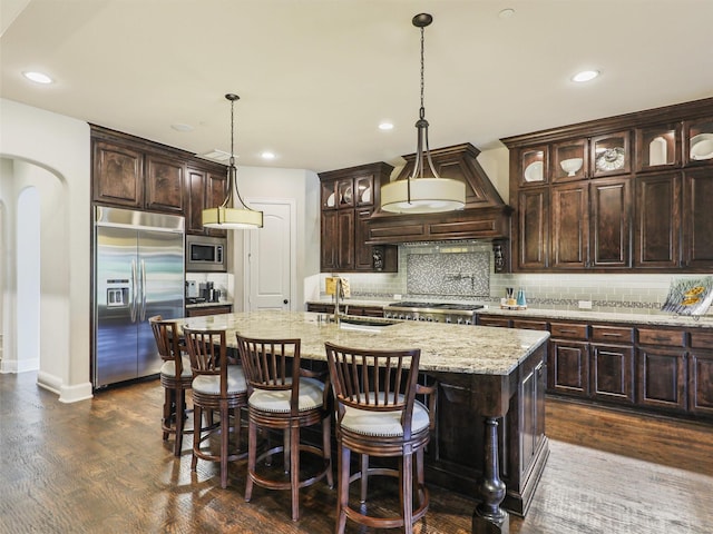 kitchen featuring sink, dark hardwood / wood-style floors, built in appliances, an island with sink, and dark brown cabinets