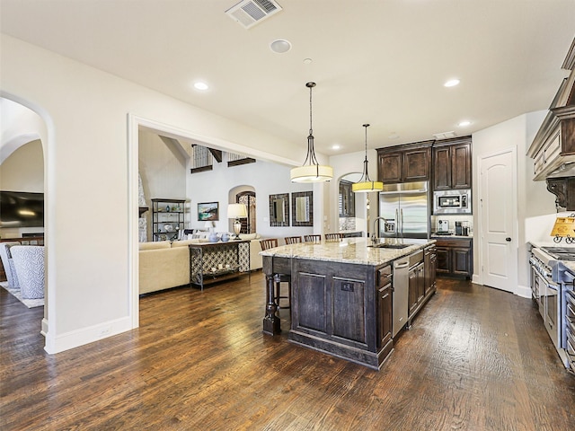 kitchen featuring dark brown cabinetry, built in appliances, dark hardwood / wood-style flooring, and a kitchen island with sink