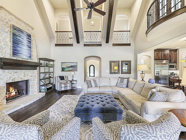 living room with beam ceiling, a stone fireplace, dark wood-type flooring, and a high ceiling