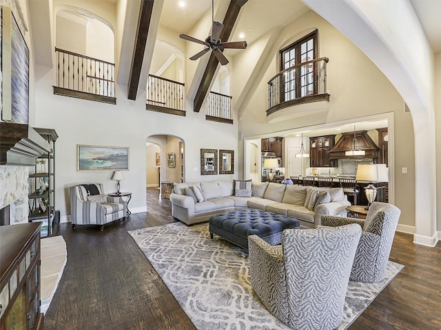 living room with ceiling fan, a fireplace, a towering ceiling, and dark wood-type flooring