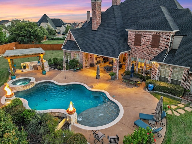 pool at dusk with an in ground hot tub, a bar, a patio, and exterior kitchen