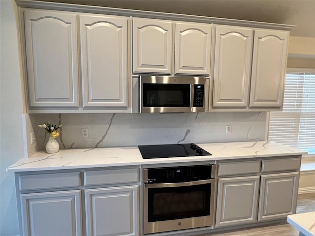 kitchen with backsplash, light stone counters, light wood-type flooring, and appliances with stainless steel finishes