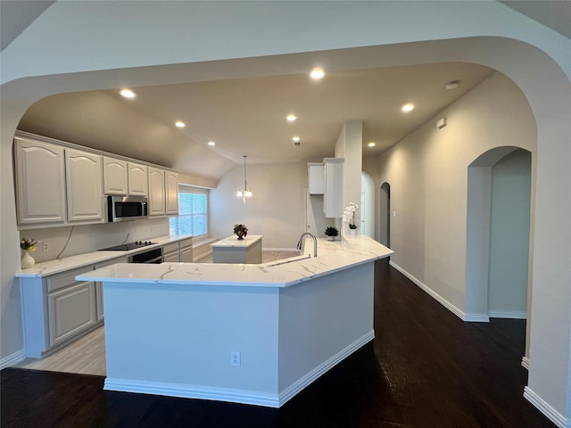 kitchen featuring hanging light fixtures, light stone counters, hardwood / wood-style floors, vaulted ceiling, and white cabinets