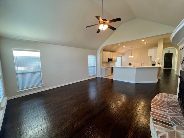 unfurnished living room featuring lofted ceiling, dark wood-type flooring, sink, ceiling fan, and a fireplace