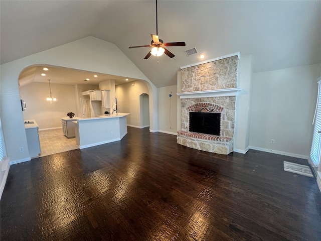 unfurnished living room featuring a fireplace, ceiling fan with notable chandelier, high vaulted ceiling, and dark wood-type flooring