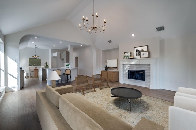 living room with hardwood / wood-style floors, a notable chandelier, a fireplace, and high vaulted ceiling