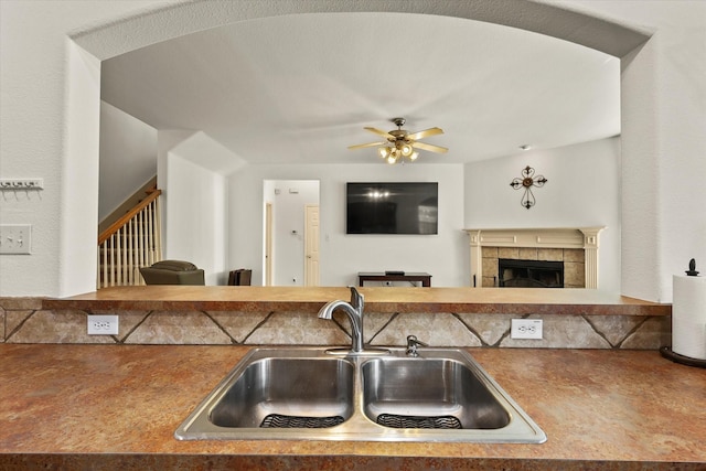 kitchen with vaulted ceiling, a tiled fireplace, ceiling fan, and sink