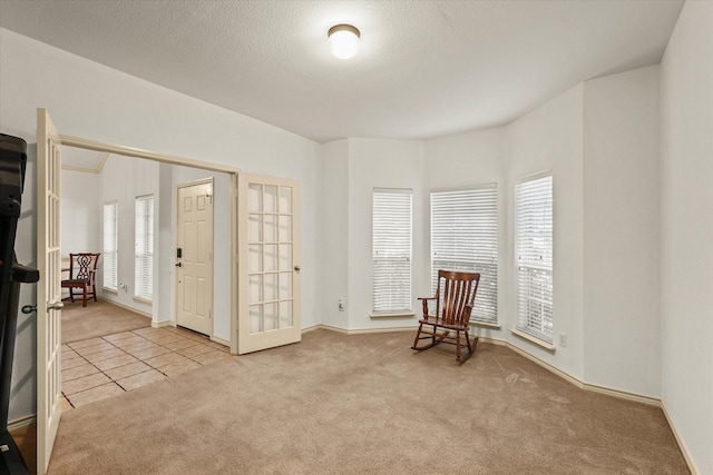 sitting room with french doors, light colored carpet, and a textured ceiling