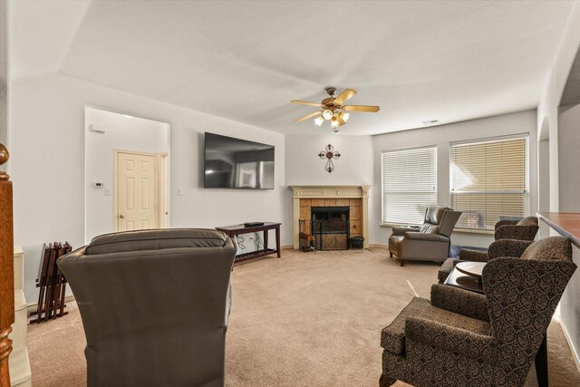 living room featuring a tile fireplace, light carpet, and ceiling fan